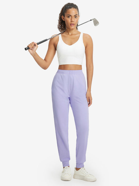 Model holding golf club behind neck while wearing lightweight women's stretchy joggers sweatpants in lavender purple.