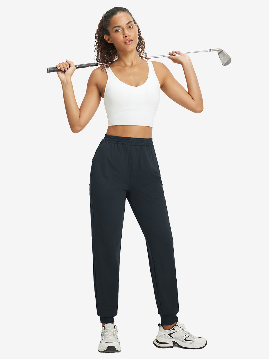 Model holding golf club behind neck while wearing lightweight women's stretchy joggers sweatpants in dark grey.
