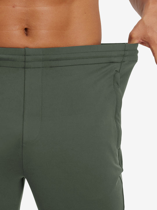 Model stretching waistband to show fit of lightweight traning track pants in olive green.