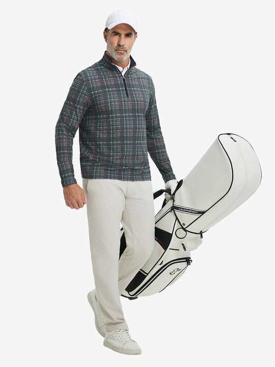 Full-body shot of model holding golf bag, dressed in full print quarter zip pullover in retro black/red plaid.