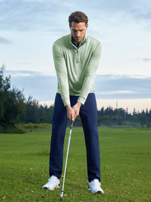 Model on grass under blue sky, leaning on golf club, wearing quarter zip melange pullover in beryl green melange.