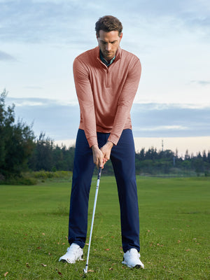 Model on grass under blue sky, leaning on golf club, wearing quarter zip melange pullover in brick melange.