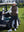 Model leaning on a golf cart, wearing coffee brown women's lightweight slim-fit puffer vest with one hand in pocket.